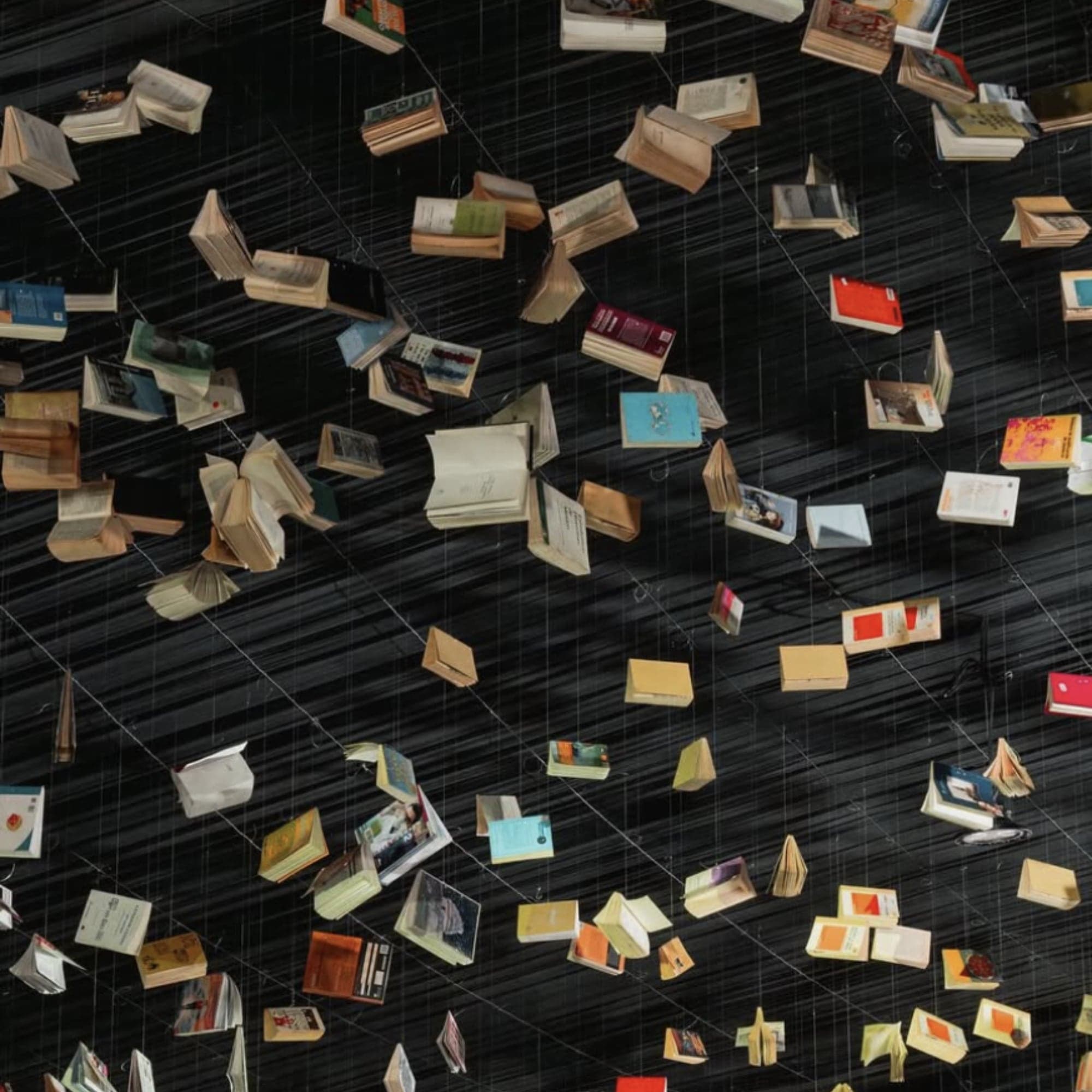 Instalación de cientos de libros abiertos suspendidos en el aire sobre un fondo oscuro