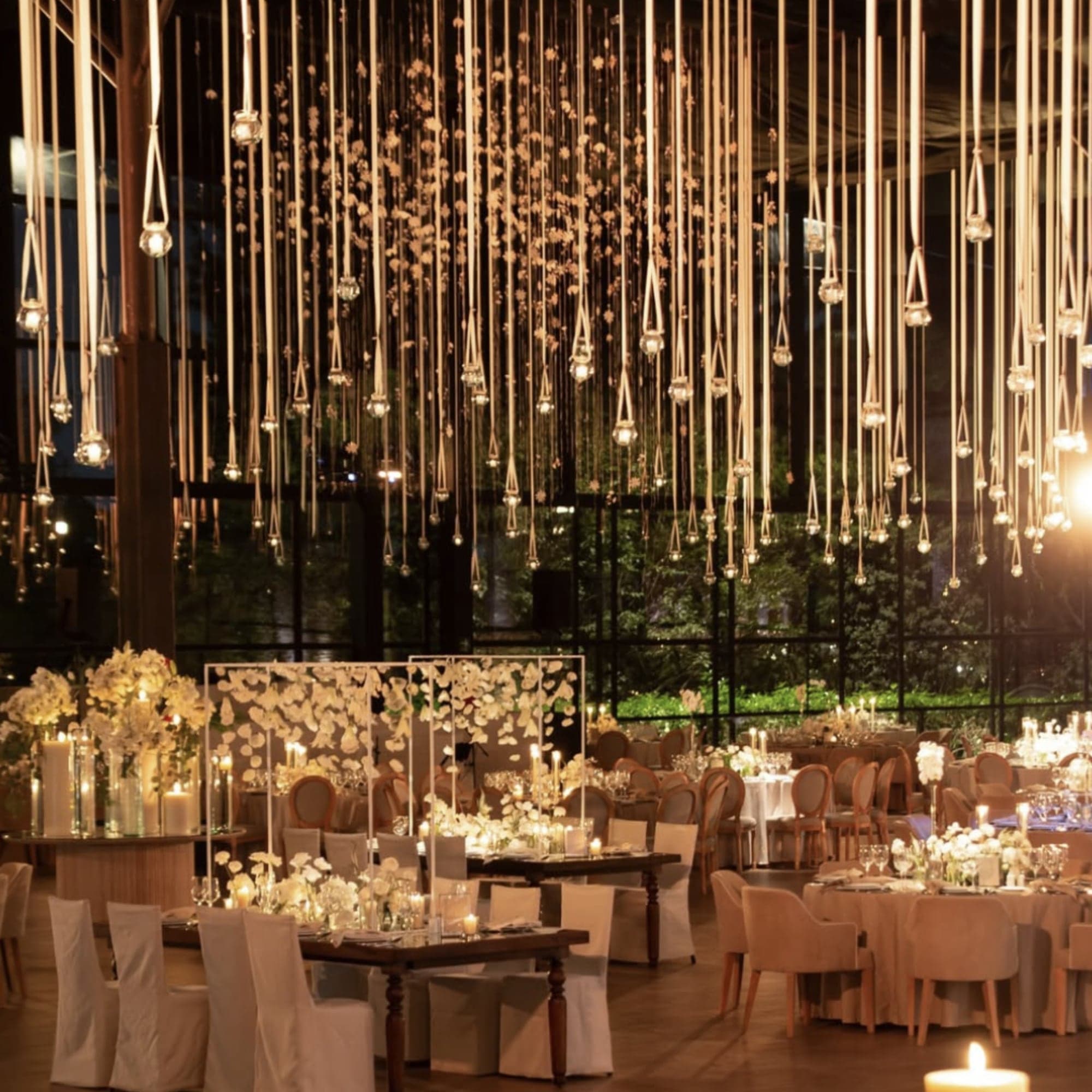 Salón de recepción con cascadas de faroles de vidrio colgantes, flores blancas y velas
