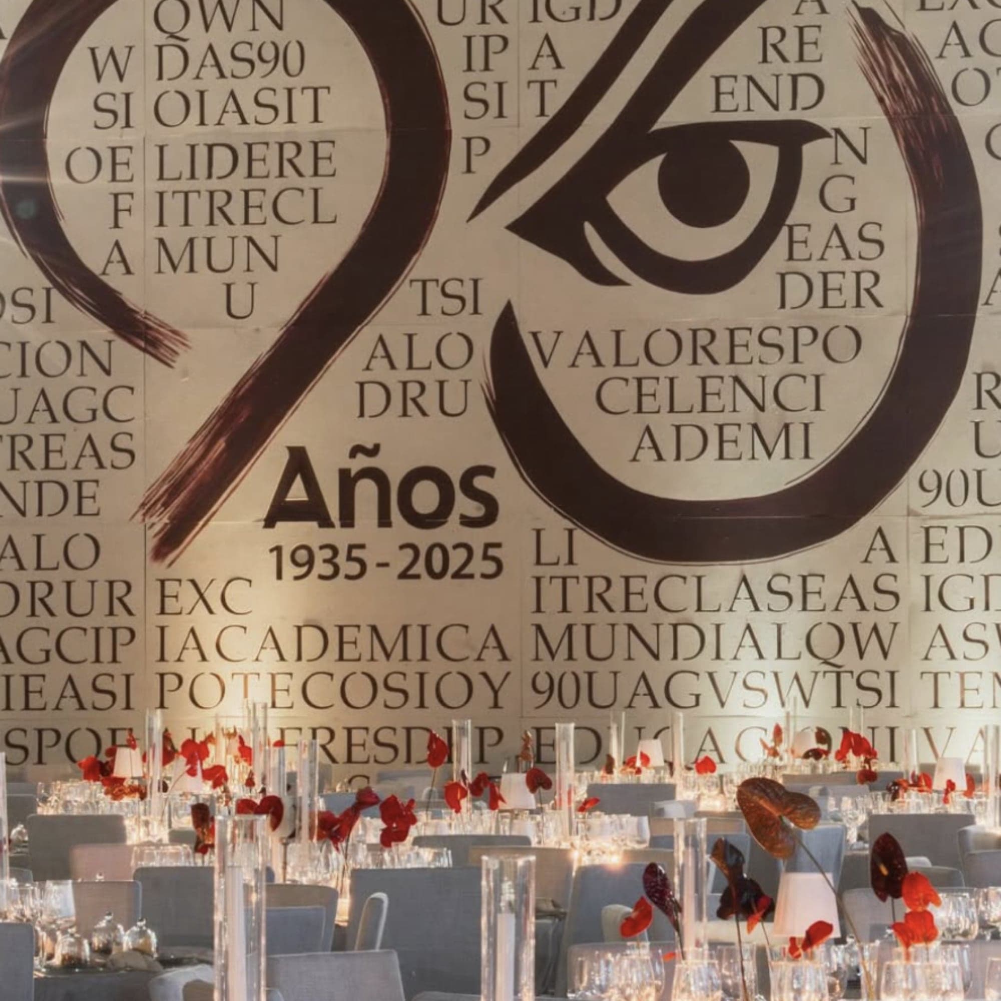 Cena de gala con centros de anturios rojos frente a un gran mural caligráfico de aniversario