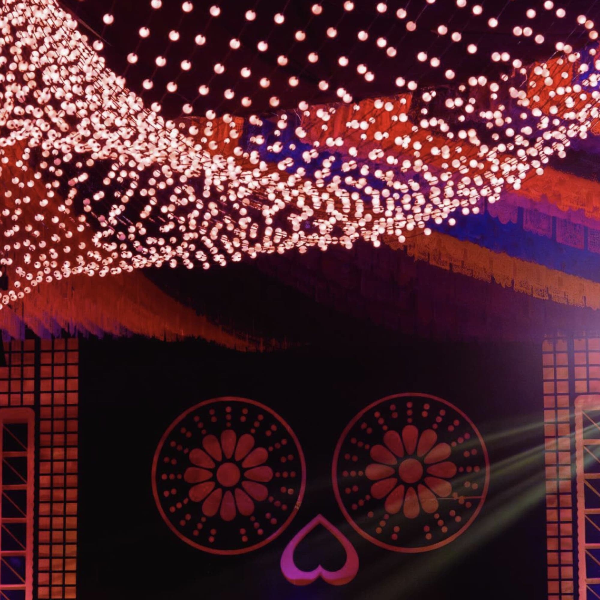 Escenario nocturno con cortinas de luces, flecos de colores y un gran motivo de calavera floral
