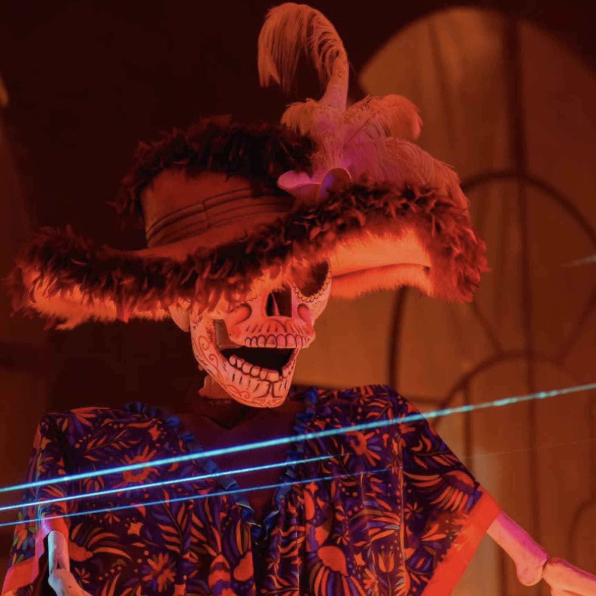 Catrina gigante con sombrero de plumas y poncho bordado bajo luces rojas en un espectáculo