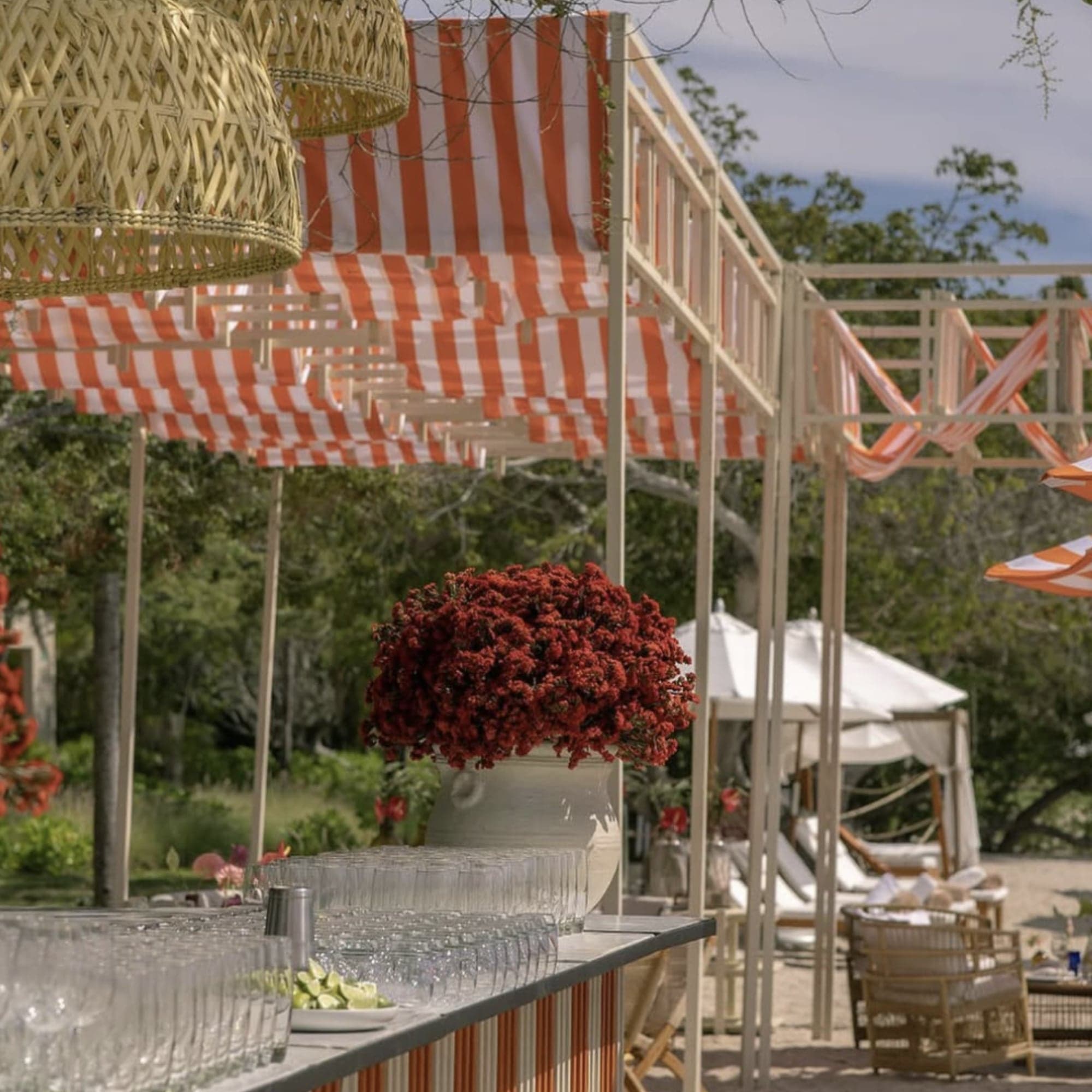 Barra al aire libre con toldos a rayas naranjas y blancas, lámparas de mimbre y flores rojas