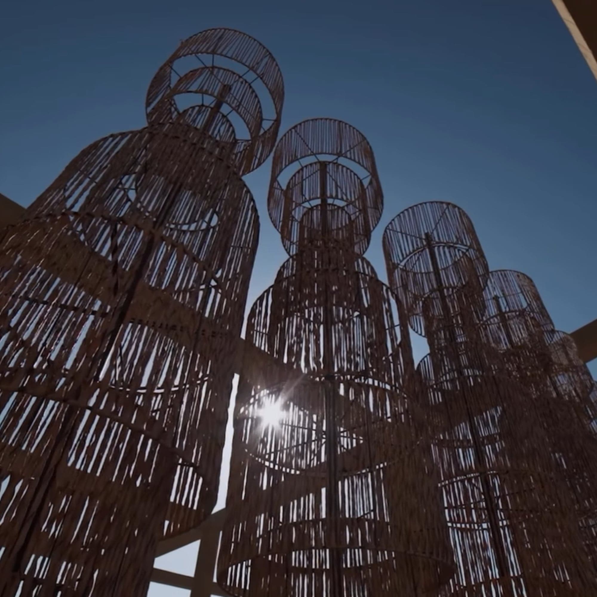 Altas esculturas tejidas en fibra natural que filtran el sol bajo un cielo azul intenso
